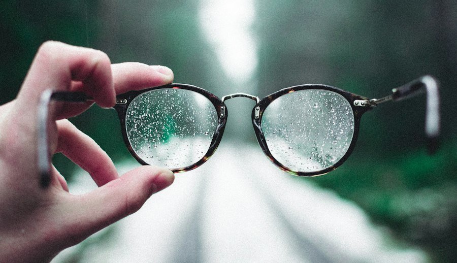 Hand holding eyeglasses with water droplets on the lenses